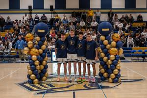 four boys basketball players lined up between two balloon pillars