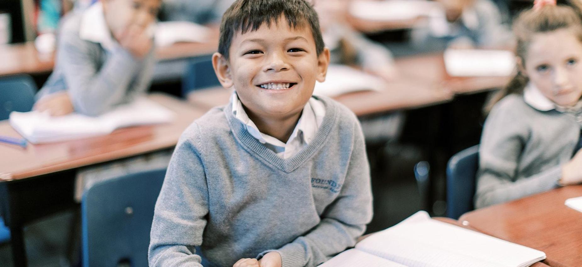 Smiling elementary student sits at his desk during class