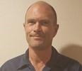 Bald man with a slight smile, wearing a dark blue shirt.