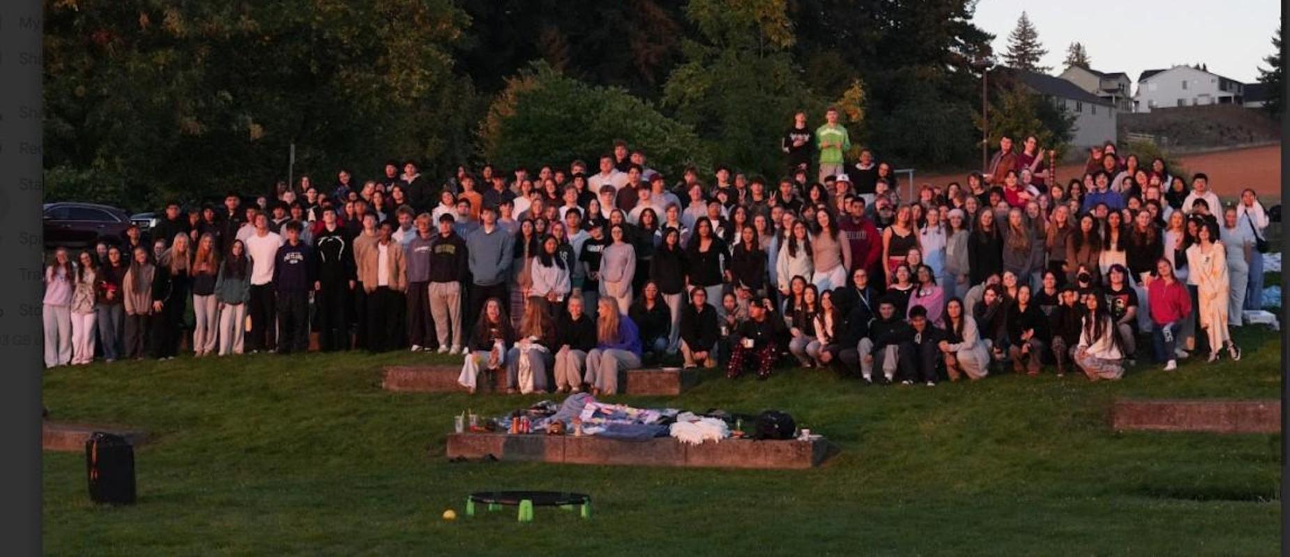 A large group of people gathered on a grassy area, posing for a photo in the evening light.
