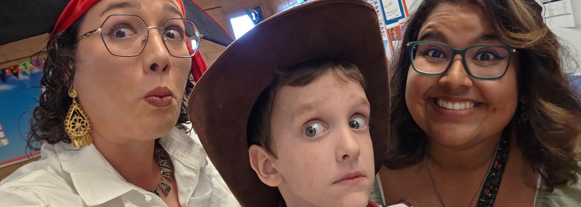 Three people making funny faces in a playful setting, with a child in a cowboy hat.