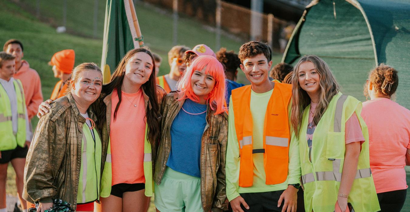 Group of friends smiling together at an outdoor event, wearing colorful attire.