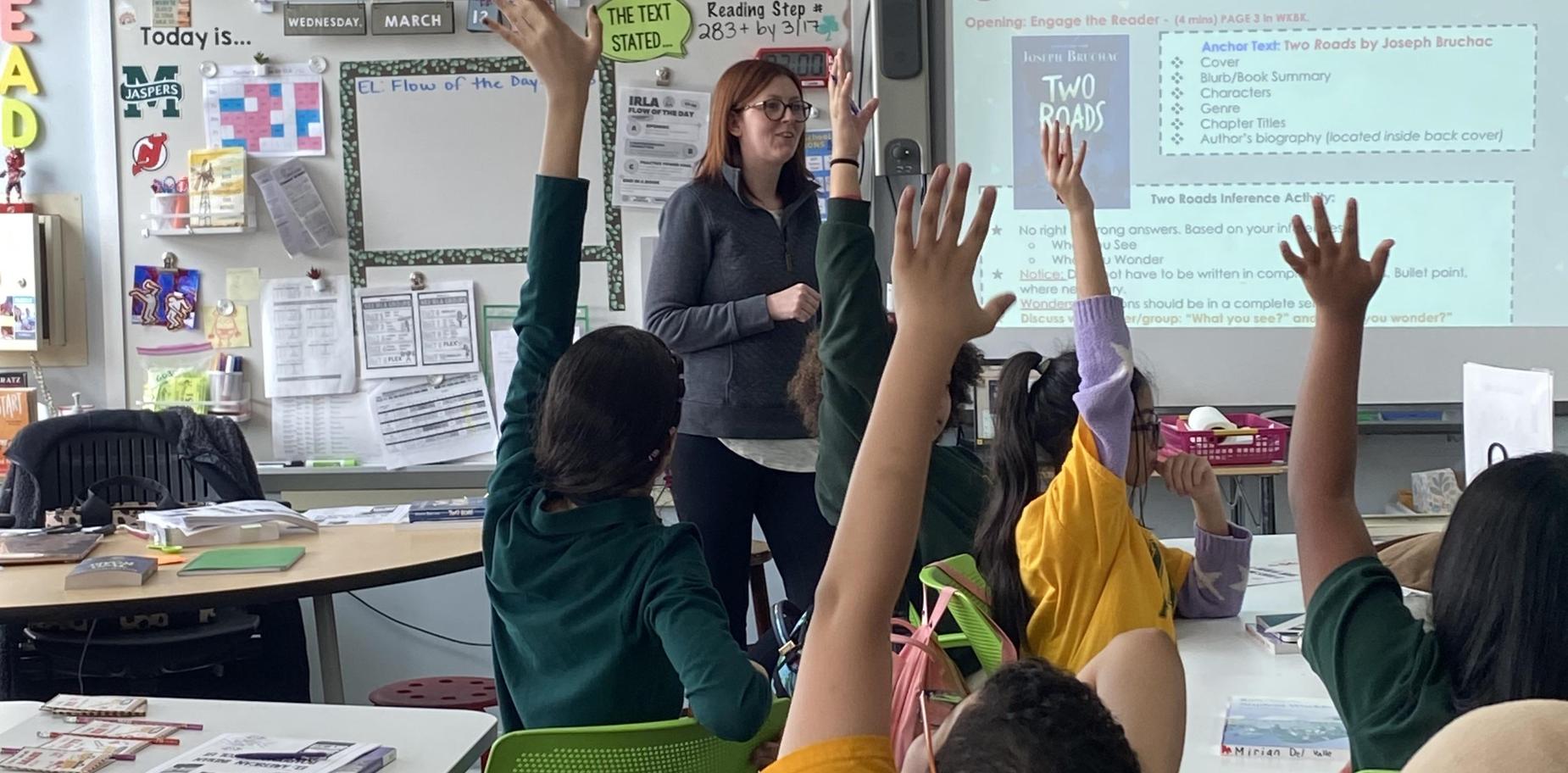 Teacher instructing students with raised hands in a classroom.