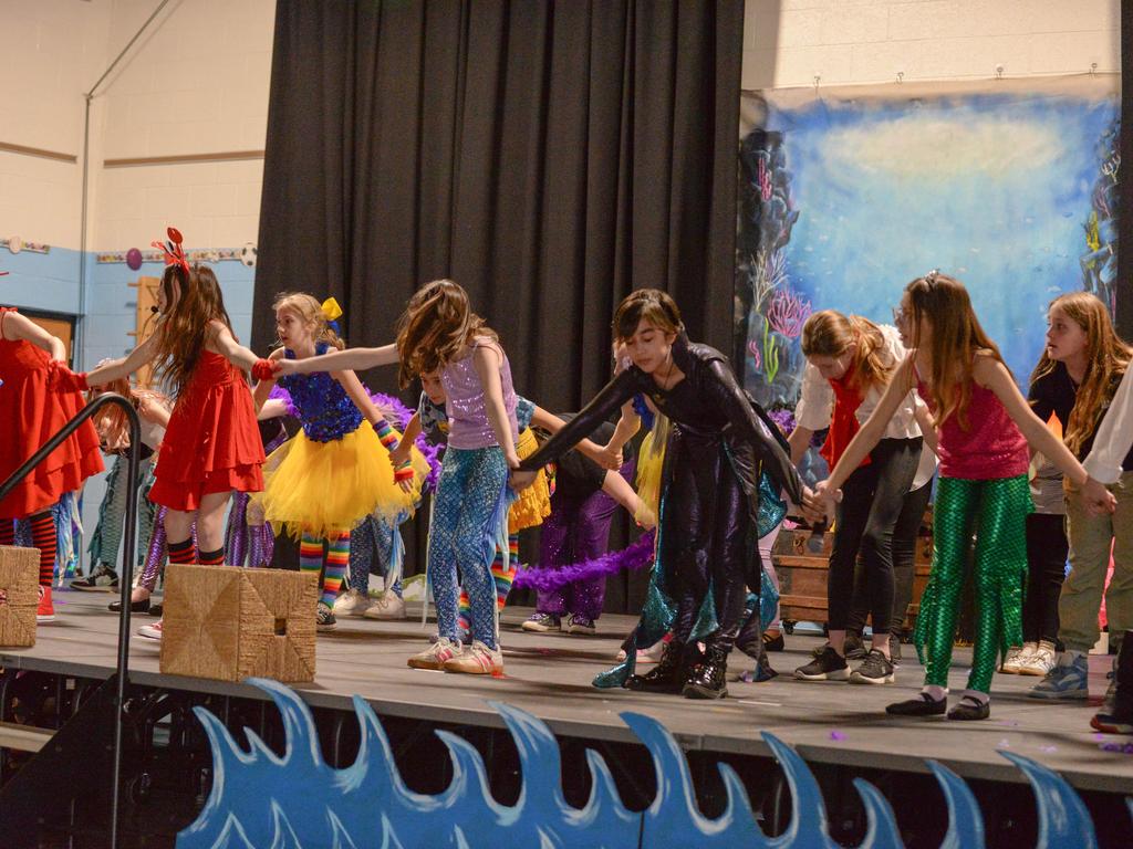 Students wearing colorful costumes on stage and taking a group bow.