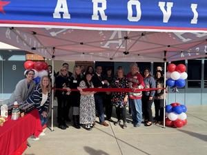 group stands under a Arovista Elementary canopy and in front of a red ribbon with scissors