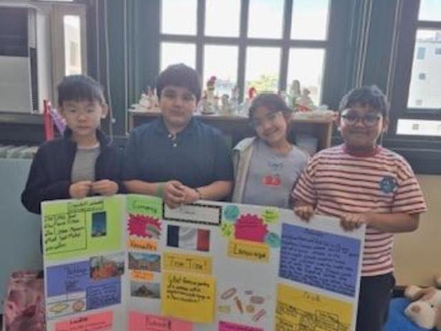Four students proudly hold a colorful poster displaying various topics.