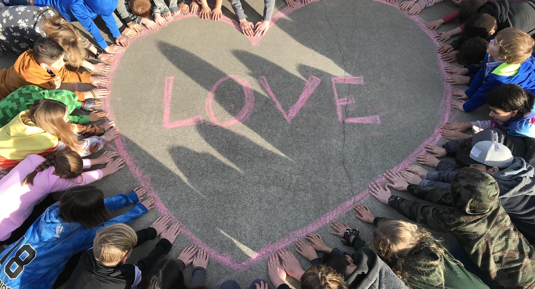 Picture of students with their hand on a giant chalk heart drawing