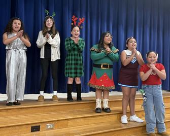 6 girls singing on stage and wearing Christmas outfits