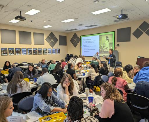 A large group of participants engaged in a workshop with tables covered in materials.