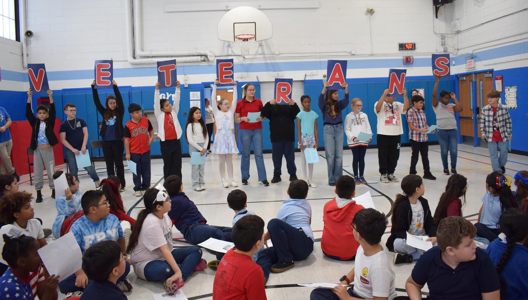 Students holding letters spelling 'VETERANS' during a presentation on a school stage.
