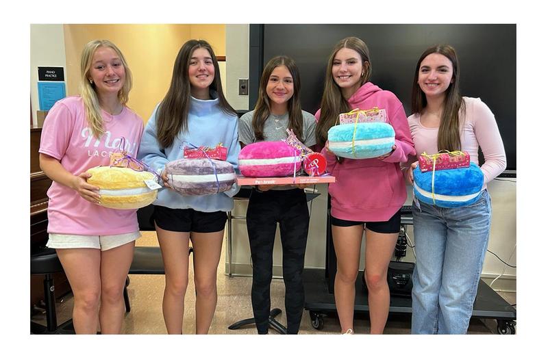 Five high school girls holding pastel colored pillows each with a wrapped present on top