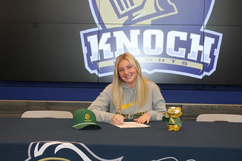 blonde hair girl smiling at camera while signing letter on table