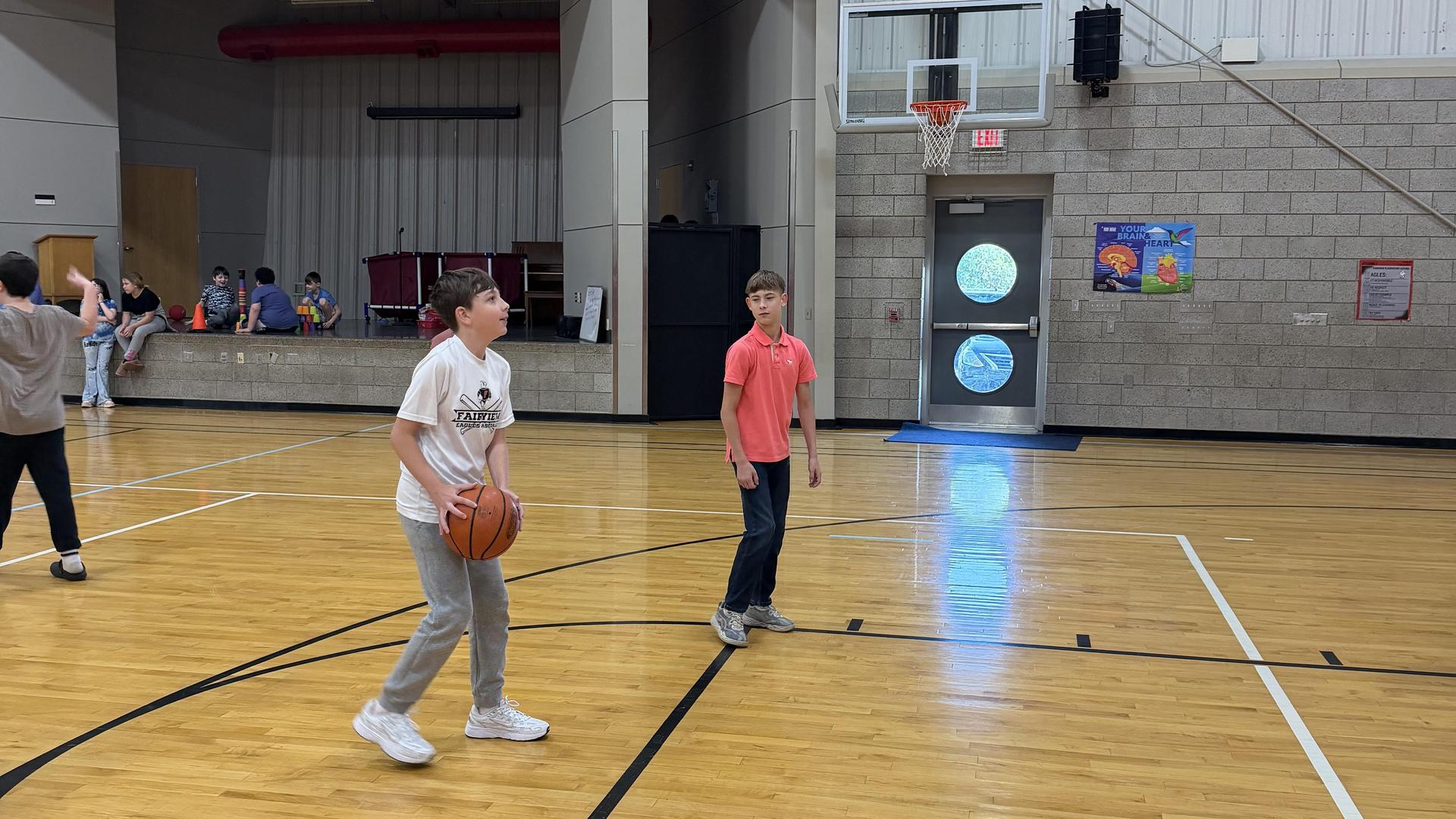 Two boys playing basketball in a gym, one preparing to shoot the ball.