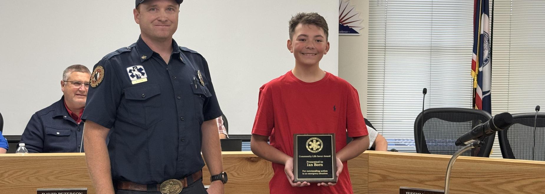 A young boy in a red shirt receives an award from a police officer at a ceremony.
