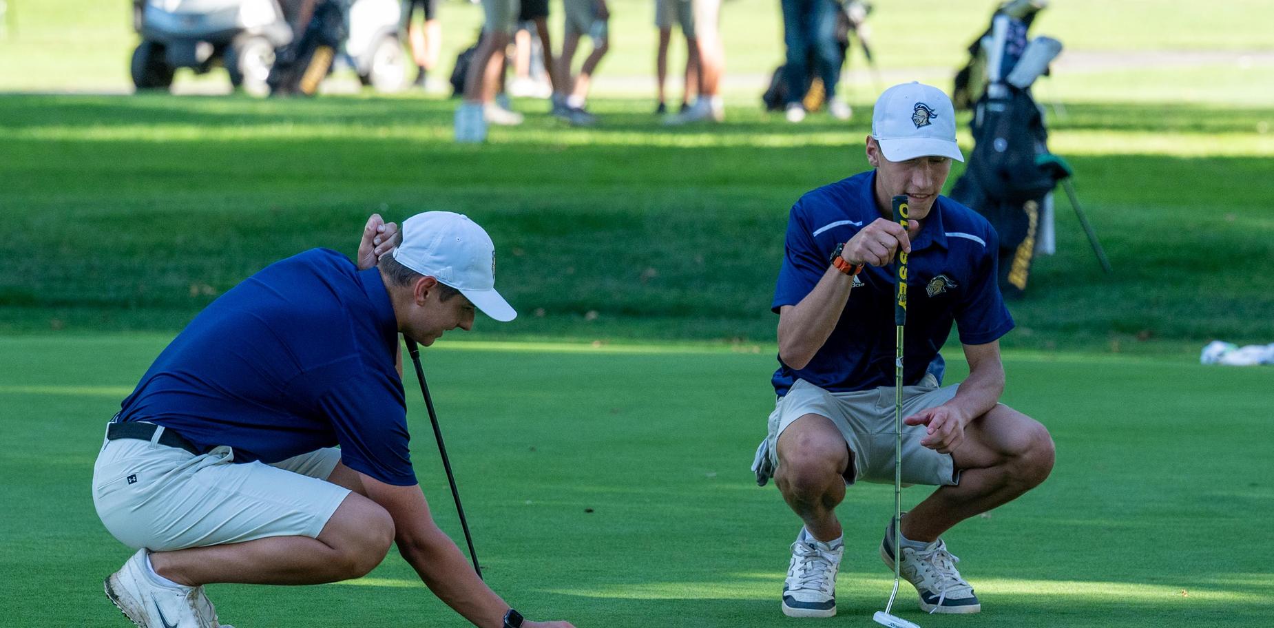Two golfers analyze the green while getting ready to putt during a game.