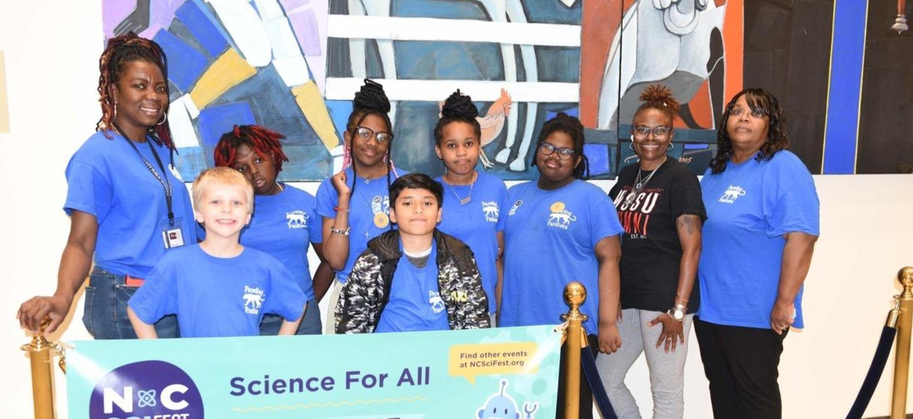 Princeville students and adults pose together behind a Science For All banner.