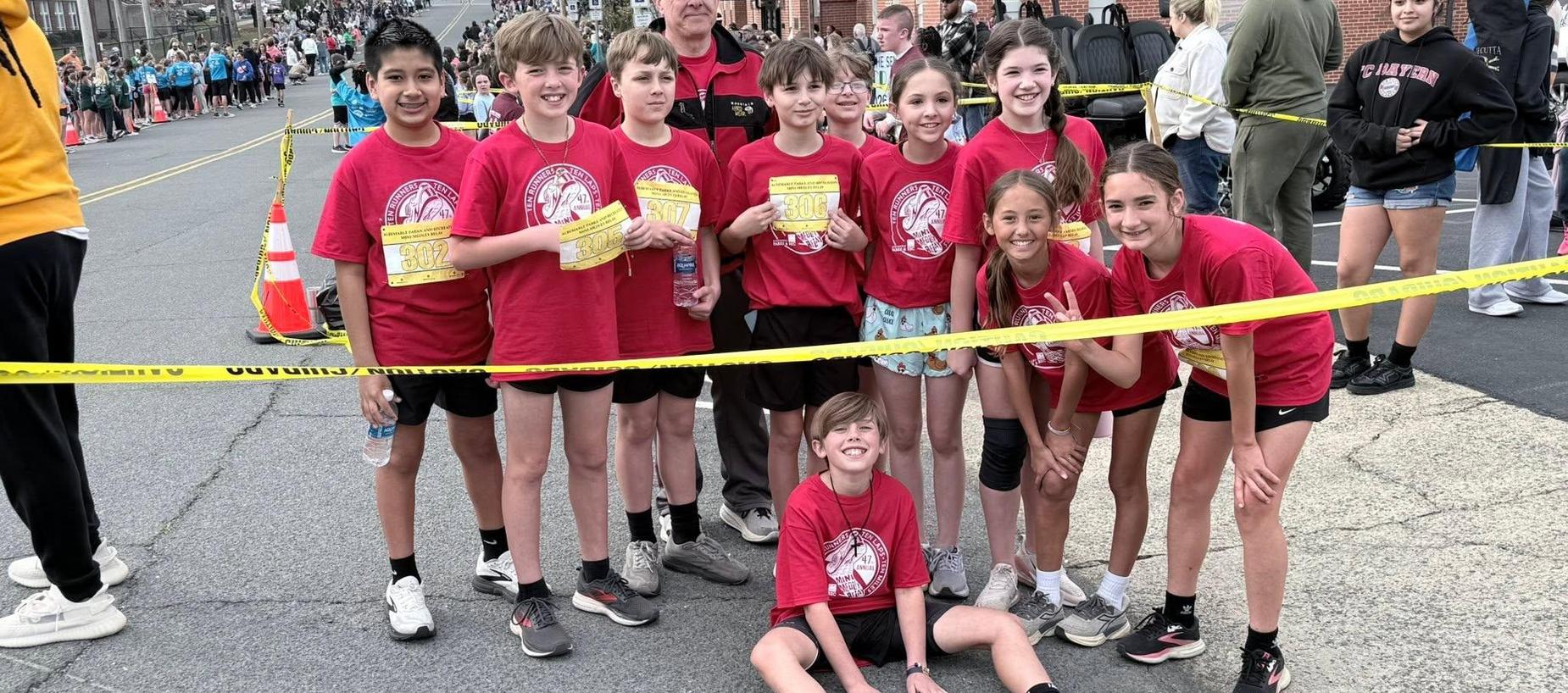 Group of children in red shirts posing together at a running event.