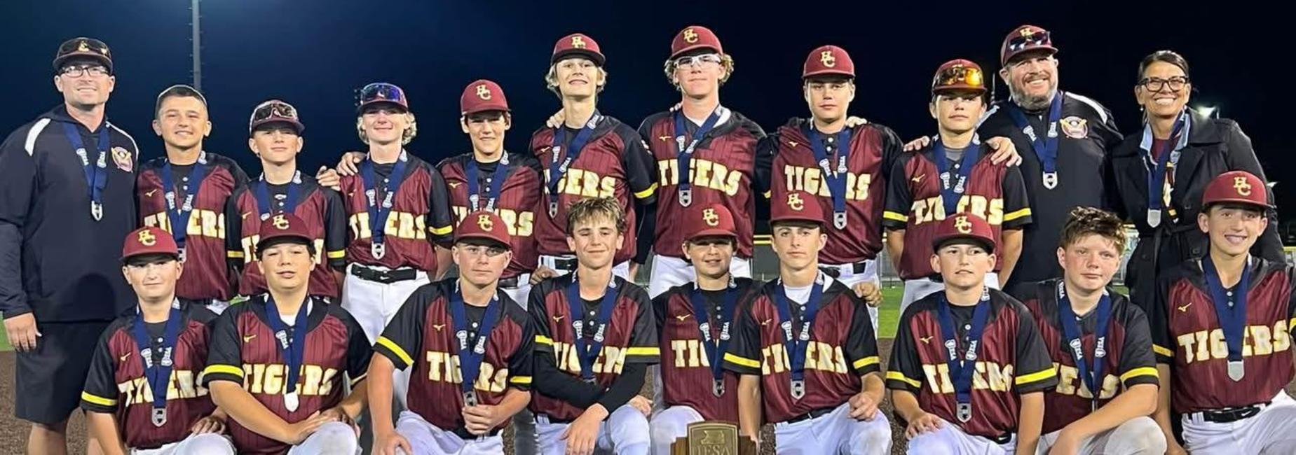 A youth baseball team poses with their trophy, wearing matching jerseys and medals.