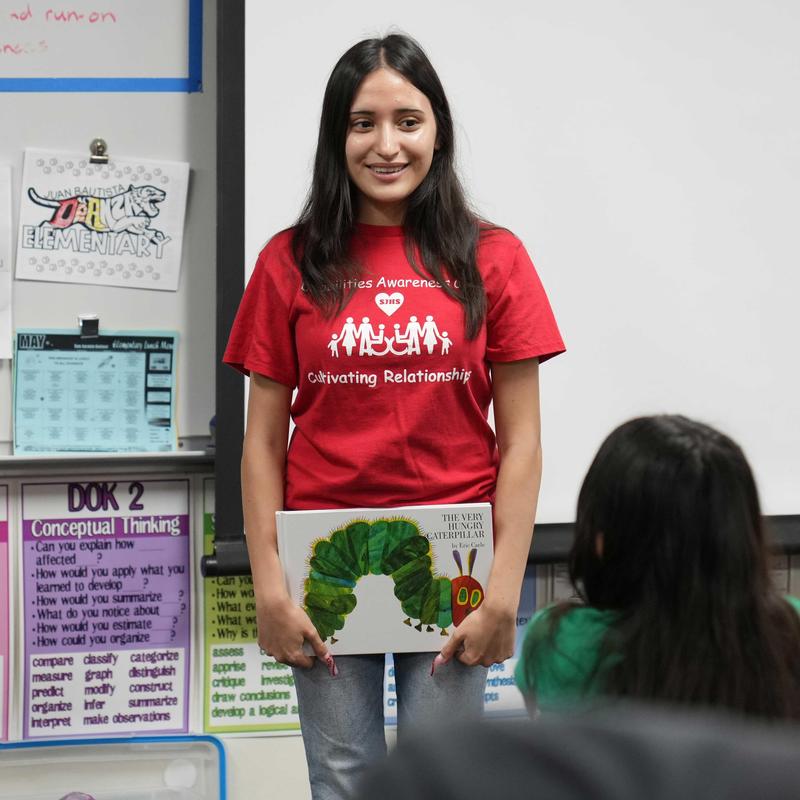 Student holding a book in front of the class