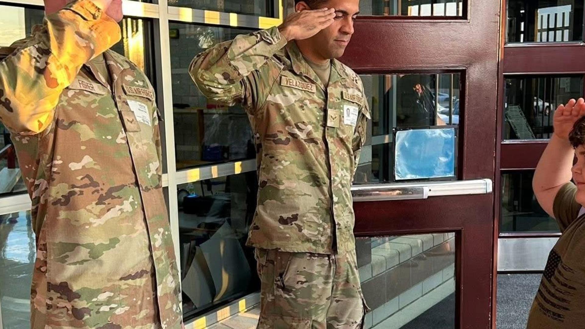 Two soldiers in uniform saluting a child at a school entrance.