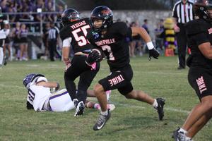 Football player running with the ball, teammates on the field in the background.