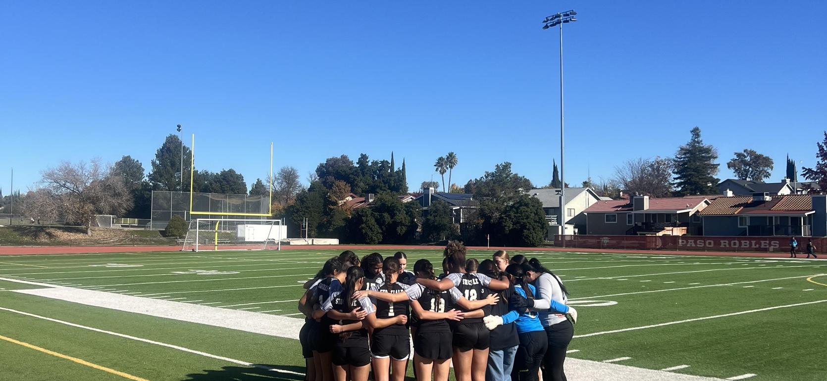A group of athletes huddling together on a sports field under a clear blue sky.