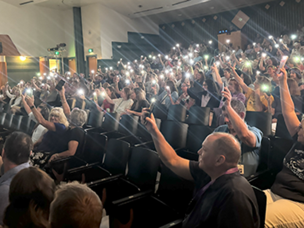 People sitting in an auditorium shining lights with their phones.