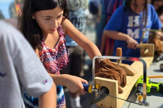 Child using tools for woodworking at a hands-on workshop.