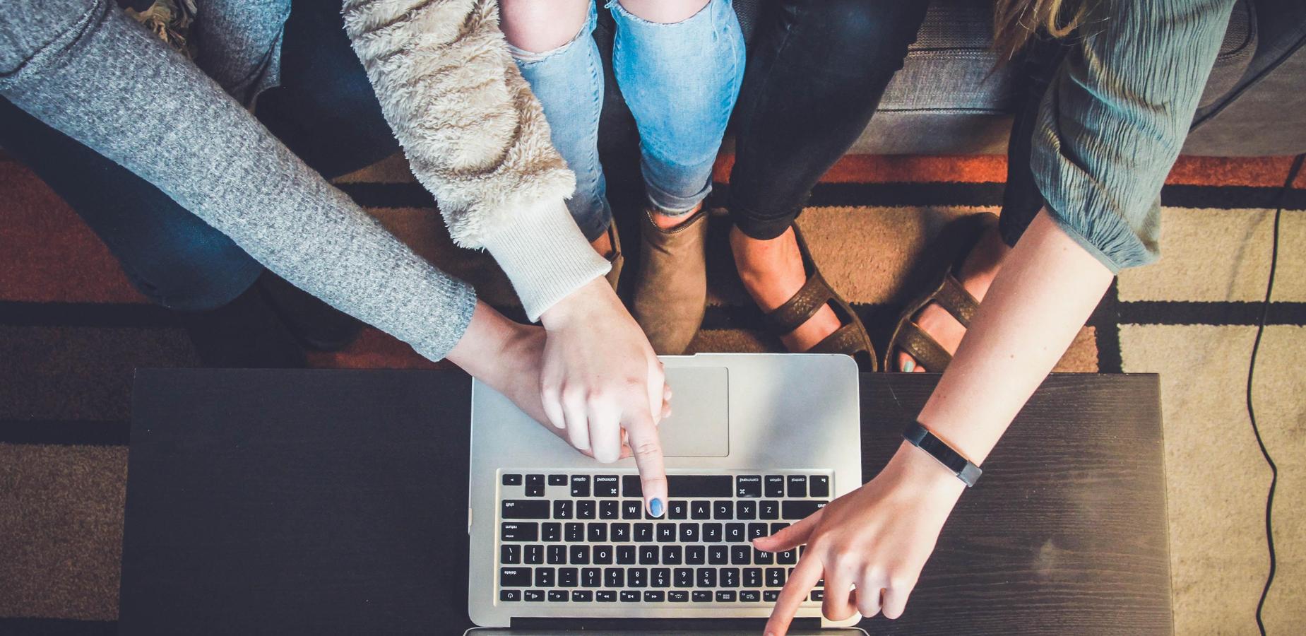 Three people pointing at a laptop during a collaborative work session.