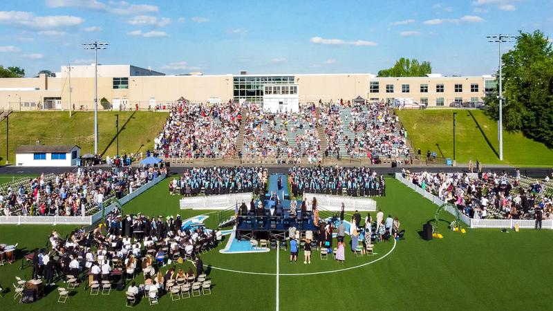 An aerial view of the class of 2026 commencement ceremony with high school in background