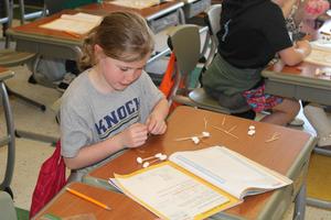 girl holding marshmallows and toothpicks looking at science book