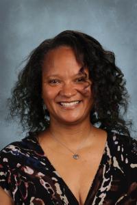 Smiling woman with curly hair wearing a patterned blouse against a gray background.