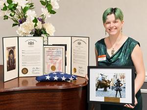 Image of a girl holding her drawing standing next to a table with her awards