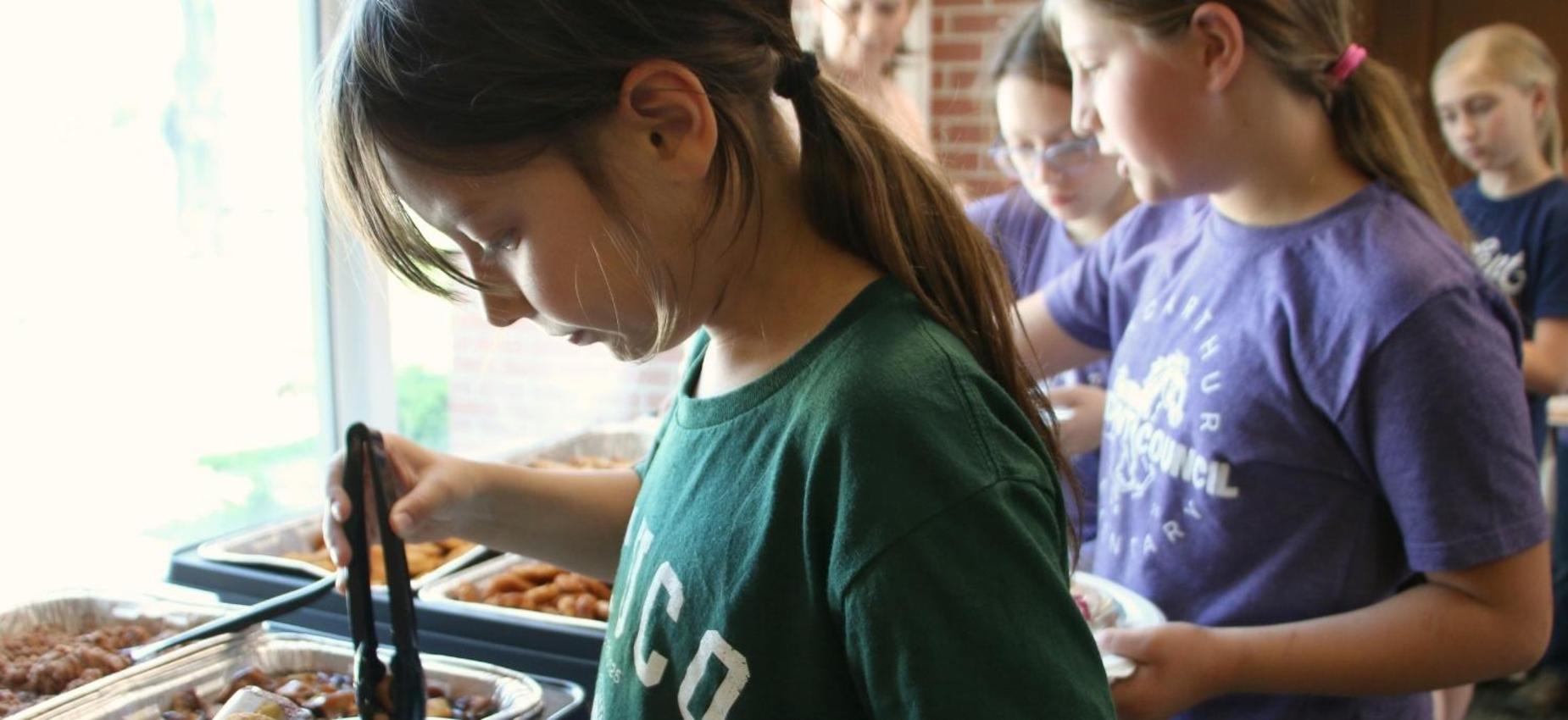 Young girl selecting food from a serving station.
