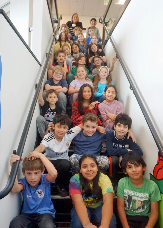 Acro Iris students smile for a class photo in a school stairwell.