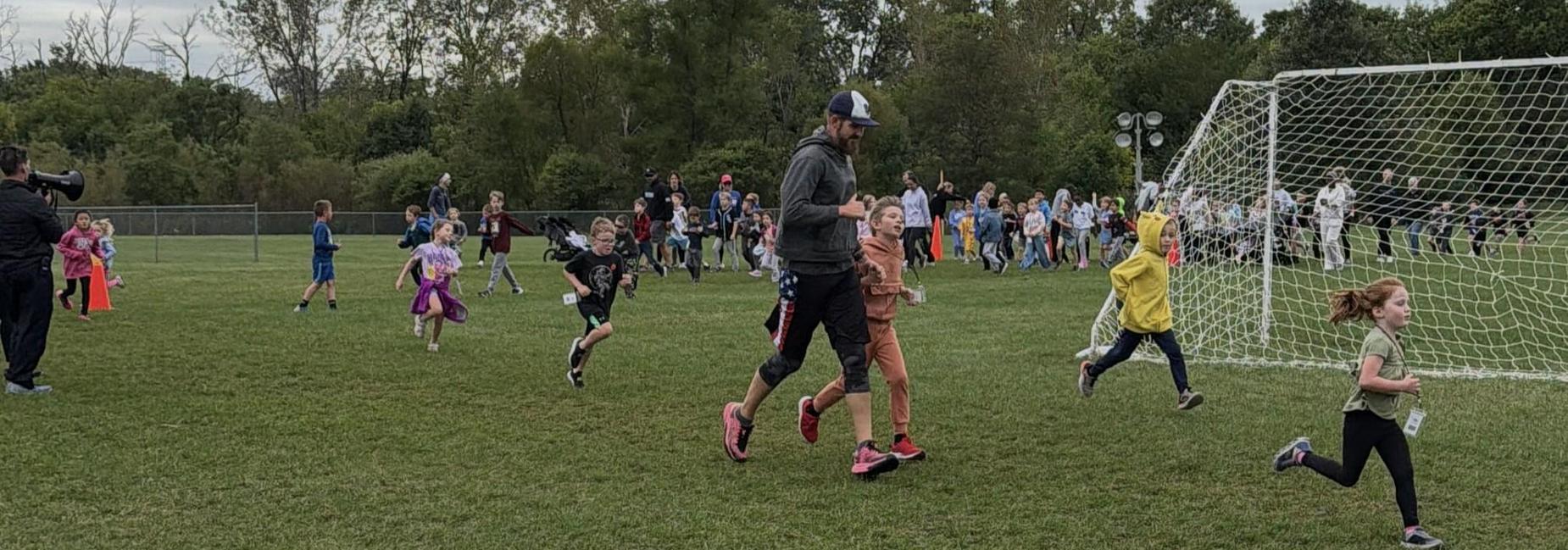 Children running on a grassy field during a sports event with a coach.