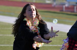 Girl in a lei catches a bubble at a sports field.