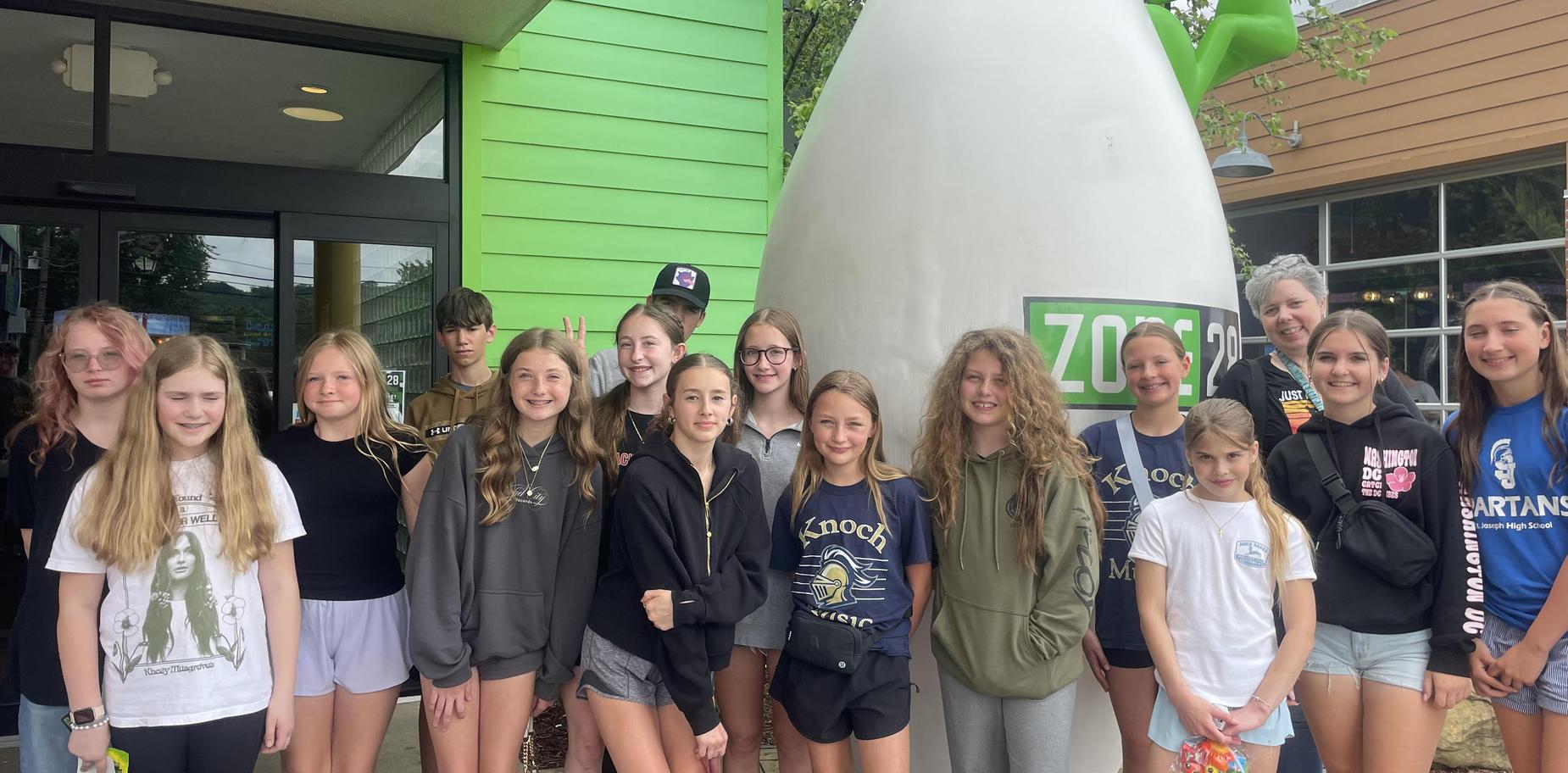 Group of girls posing outside a colorful building near a large penguin statue.