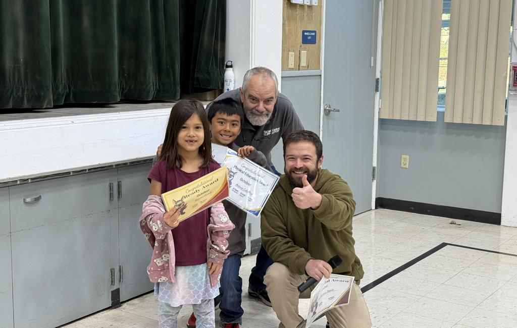 Students holding an award, teacher doing thumbs up