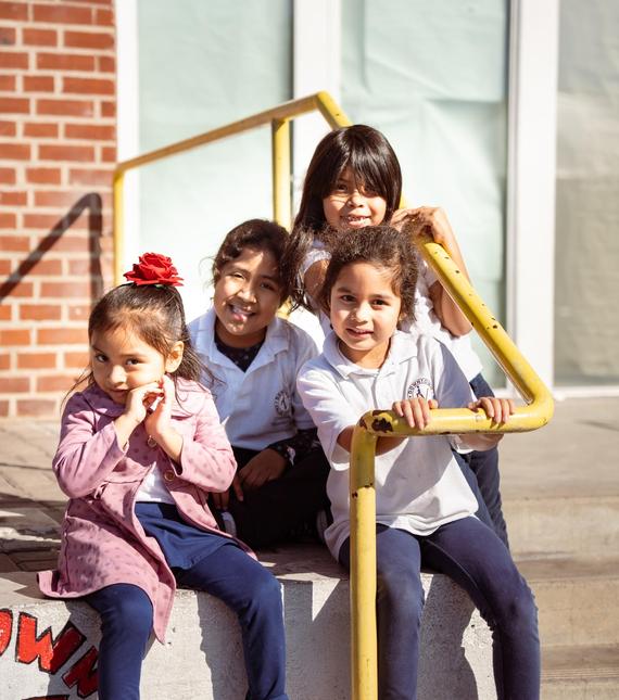 Four girls smiling and sitting on stairs, with a yellow handrail in the foreground.