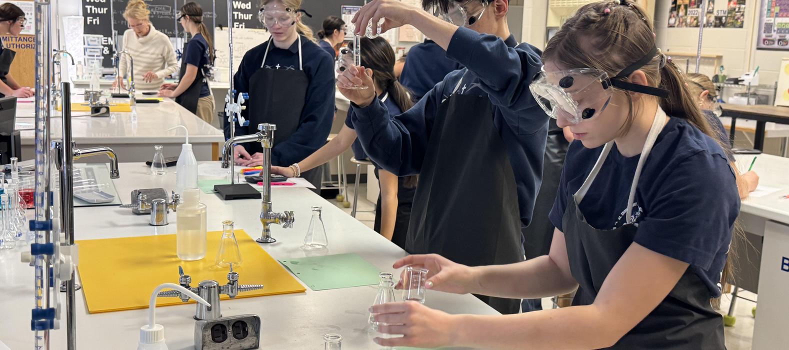 Students in lab coats conducting experiments with glassware in a science classroom.