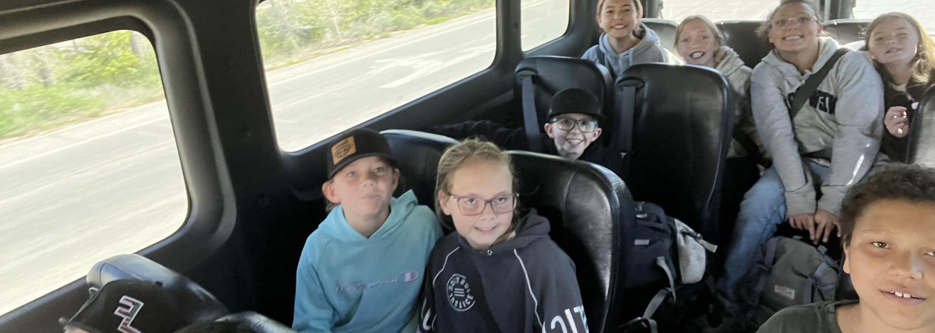 A group of children smile while seated on a bus.