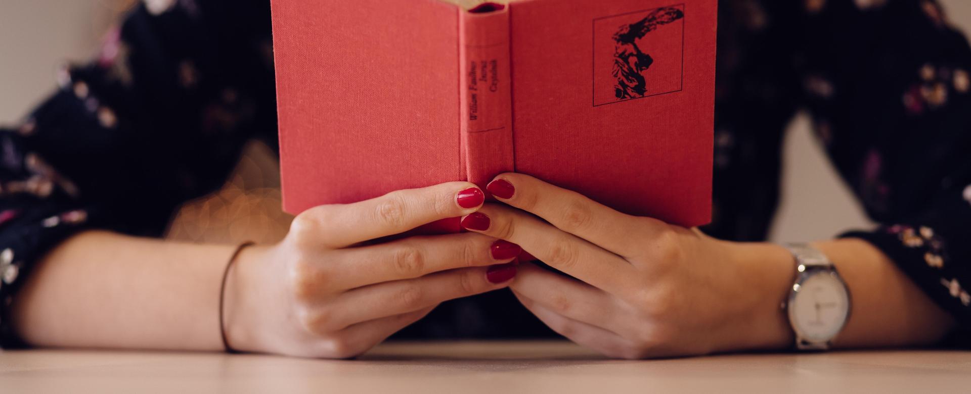 A person holds a red book open, showing the text inside.