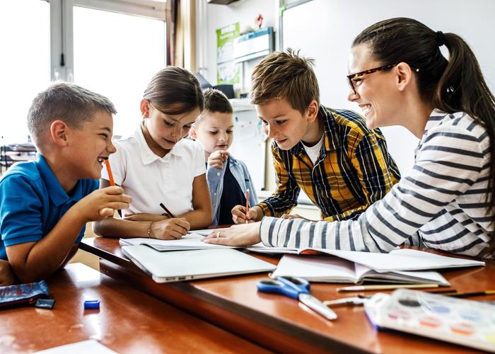 A teacher assists five children in a classroom activity.