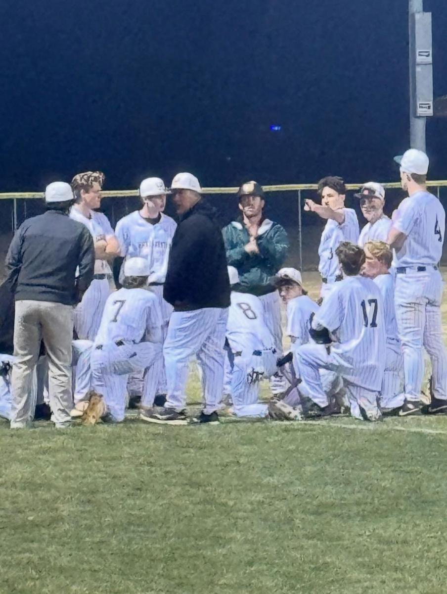 A group of baseball players and coaches gathered in a huddle on the field at night.
