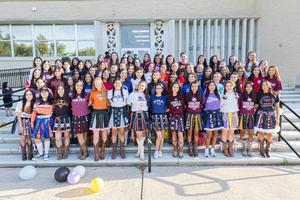 Large group of girls in colorful shirts posing on steps with balloons.