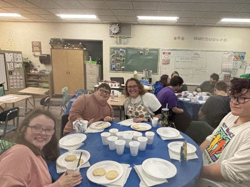 A group enjoying snacks at a table in a classroom with blue tablecloths.