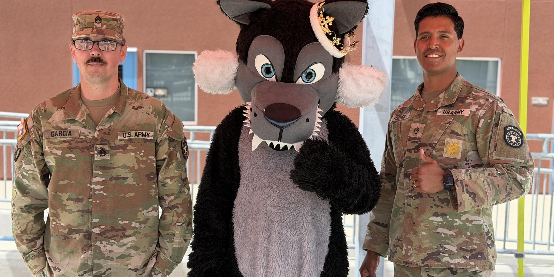 Two soldiers stand next to a large wolf mascot in a colorful setting.