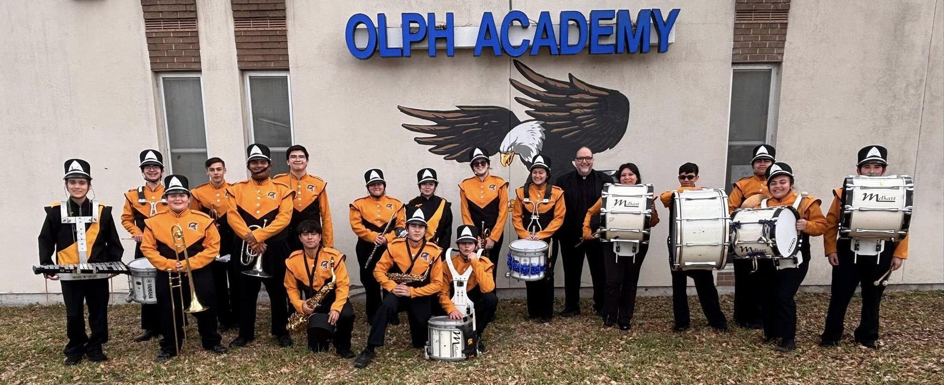 Marching band in uniforms poses in front of an eagle mural.
