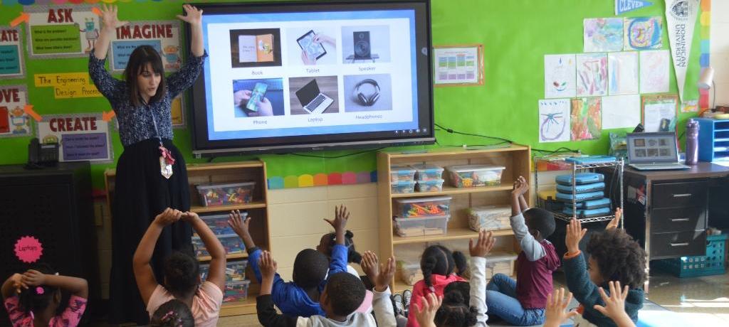 seated students mimic teacher who is raising her arms overhead